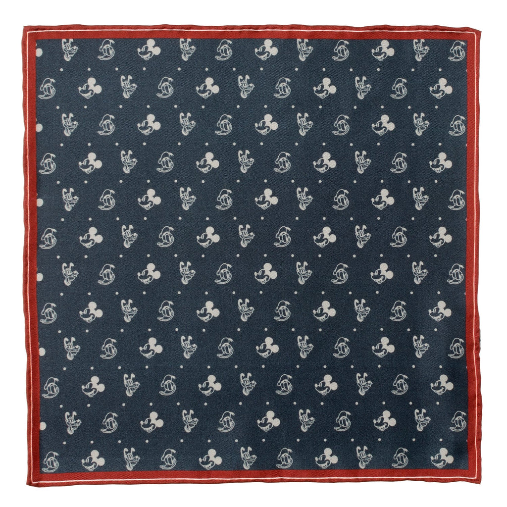 A navy silk pocket square with a white print of Mickey Mouse, Donald Duck, and Pluto with a burgundy border, displayed flat and inside a suit jacket pocket.