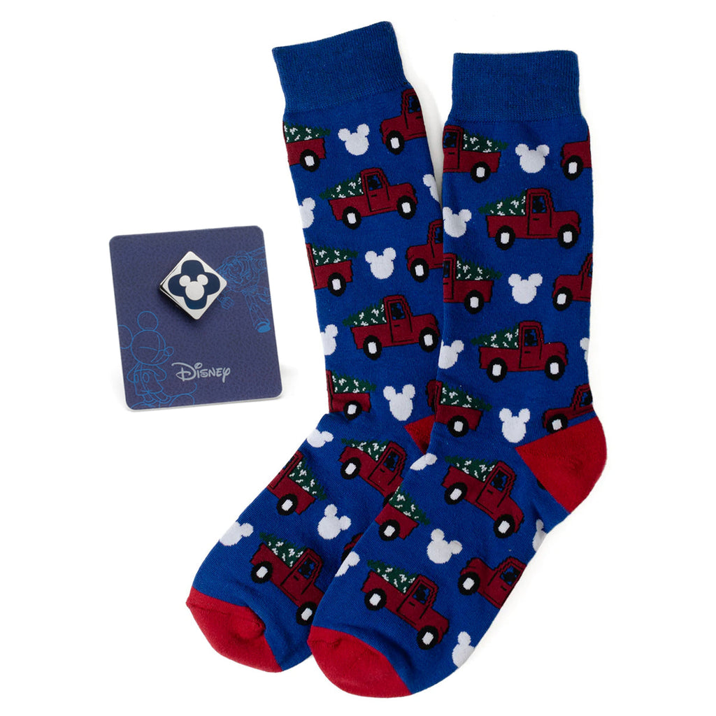 A pair of navy blue crew socks with a repeating pattern of red holiday trucks and Mickey Mouse silhouettes, accompanied by a blue Mickey Mouse enamel lapel pin.