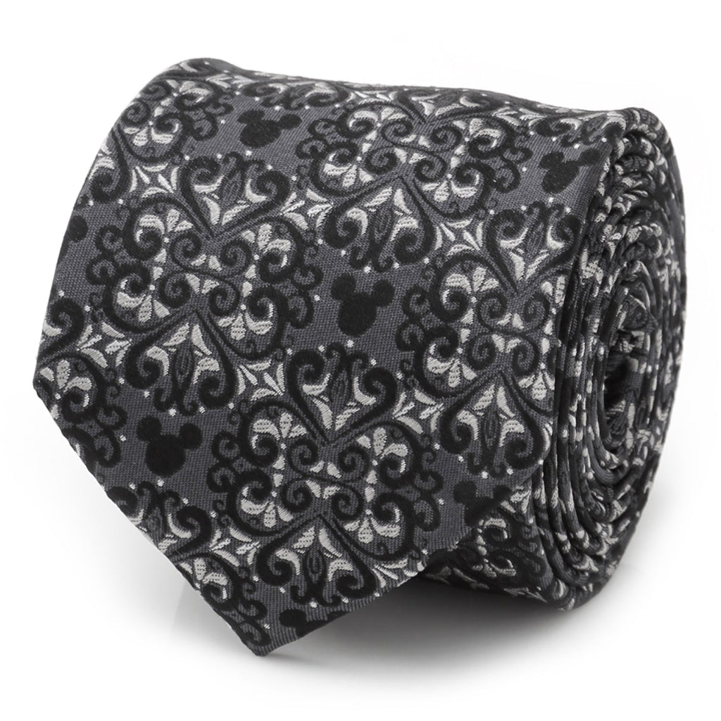 Close up of a gray and silver silk tie with a damask pattern and hidden Mickey Mouse motifs rolled on a white surface.