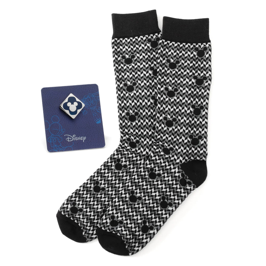 A pair of black, white, and grey chevron socks featuring a repeating Mickey Mouse icon pattern, shown next to a matching blue Mickey Mouse enamel lapel pin on a card.