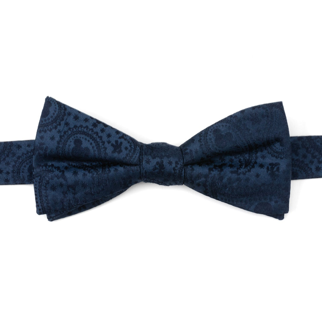 Close up of a navy blue silk bow tie featuring a subtle paisley print with Mickey Mouse head silhouettes.