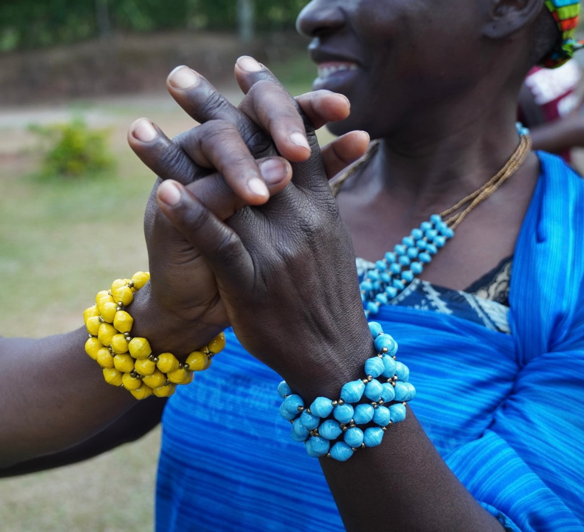 Blue and yellow Ugandan paper bead cuff bracelet with gold spacer beads on a white background.