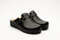 A pair of black women's genuine leather clogs featuring a side buckle and massage gel insole on a white background.