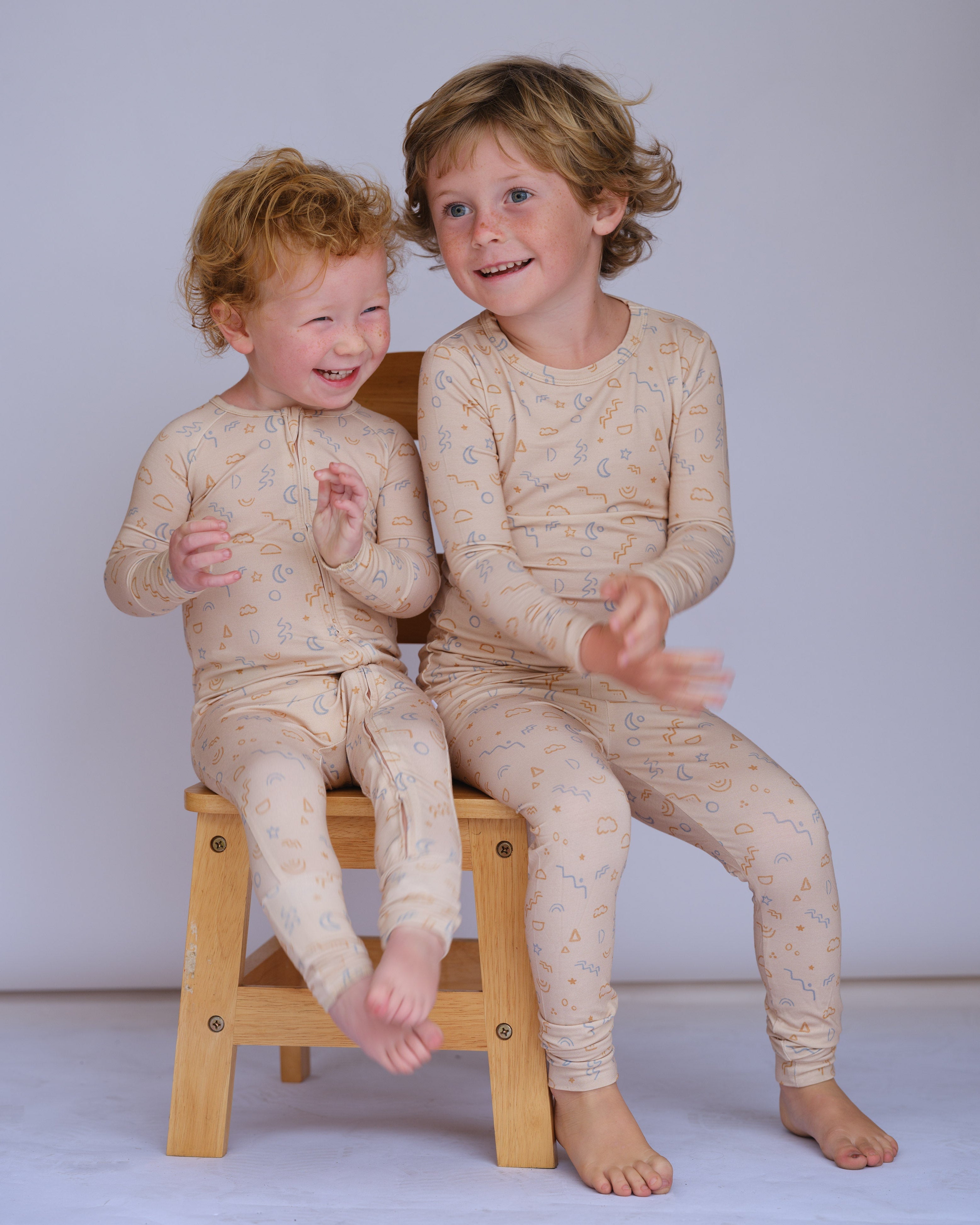 Two children wearing matching pajamas sitting on a wooden stool against a plain background
