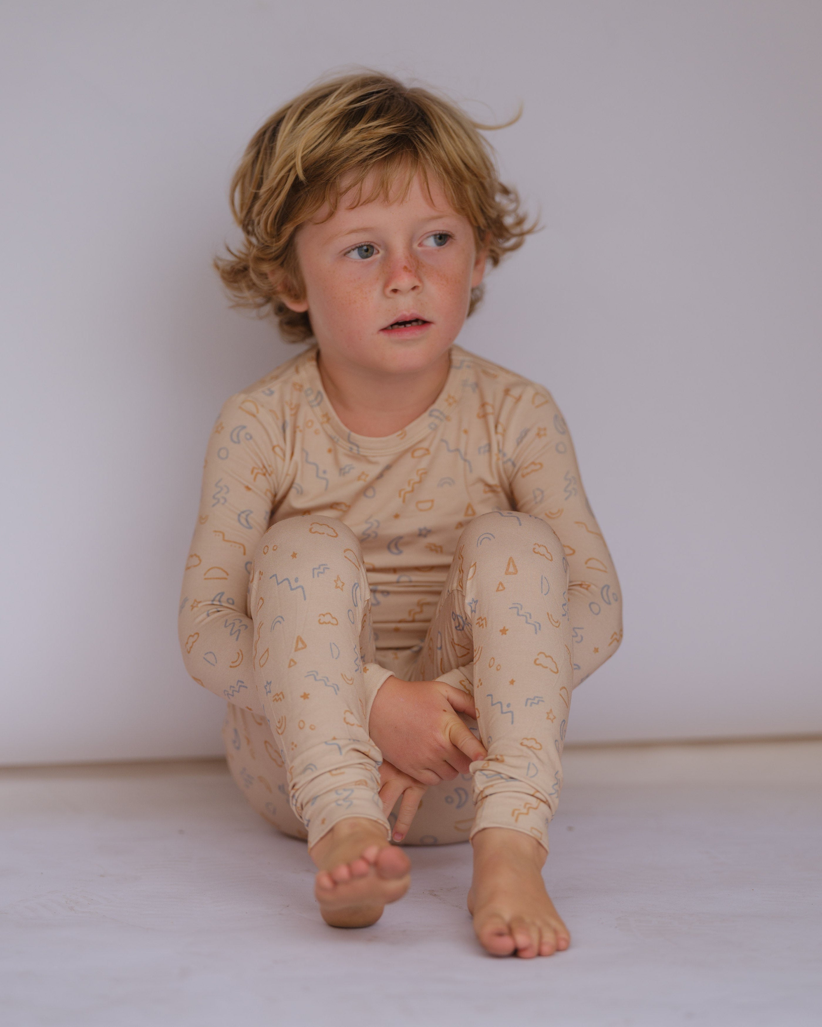 Child wearing a patterned onesie sitting on the floor against a plain background