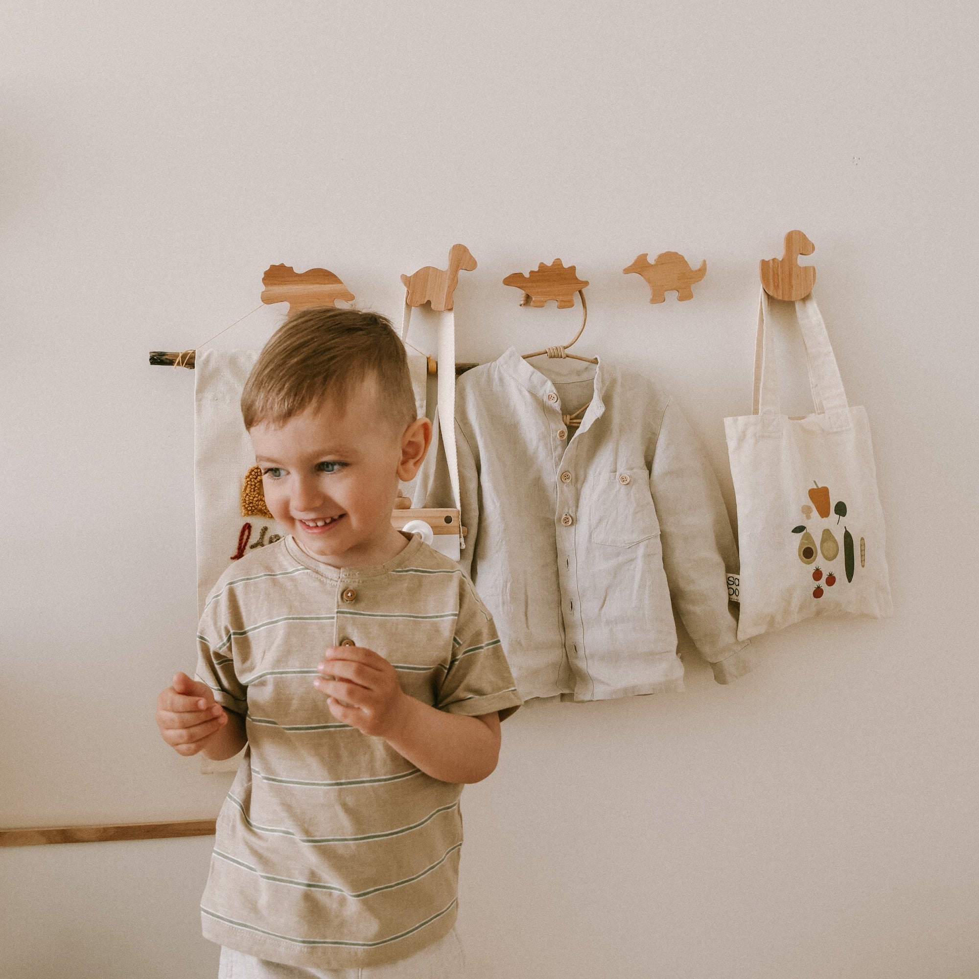 Light brown handcrafted wooden dinosaur wall hooks mounted on a white wall in a nursery.