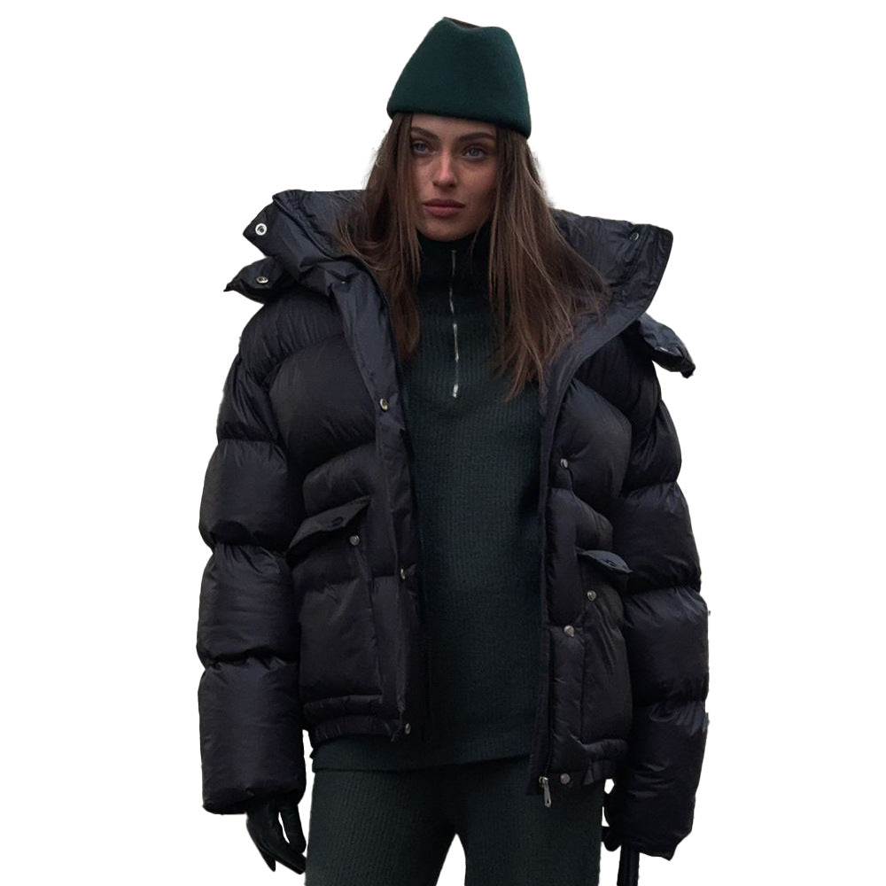 Woman wearing a black hooded puffer jacket with square pockets over a dark green outfit, looking stylish and warm.