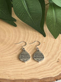 Silver drop earrings with the text With God All Things Are Possible engraved on a teardrop charm resting on a wood slice