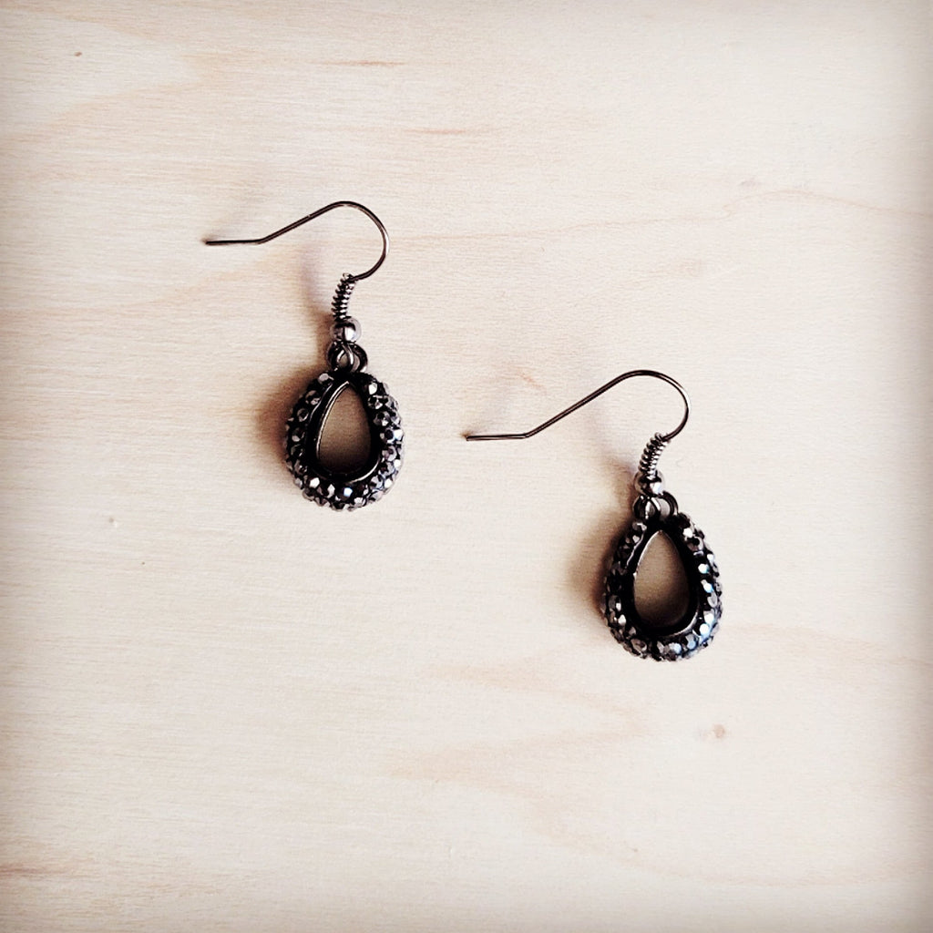 A pair of small dark teardrop-shaped dangle earrings featuring crystal accents on a light wooden background.