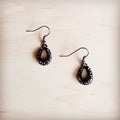 A pair of small dark teardrop-shaped dangle earrings featuring crystal accents on a light wooden background.