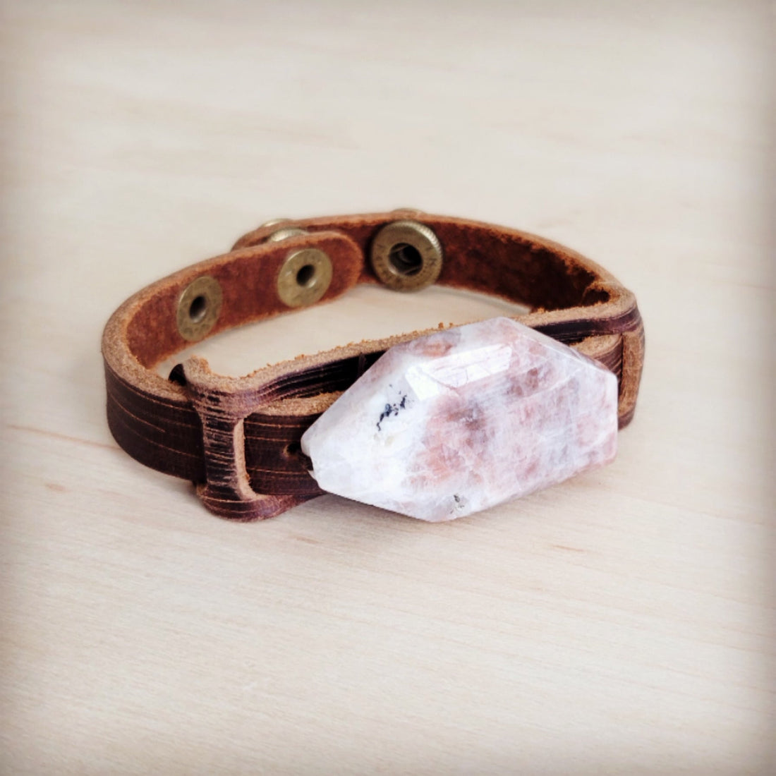 Narrow brown leather cuff bracelet featuring a large, raw-cut sunstone slab and brass-tone snap closure