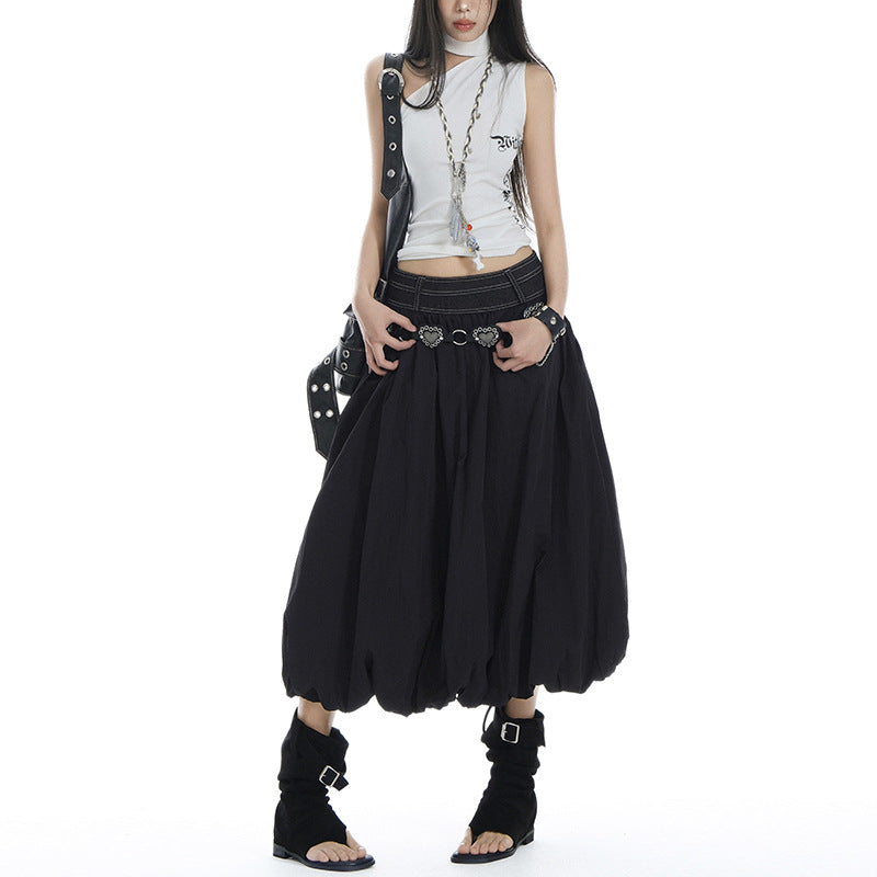 Model wearing a black elastic high waist pleated bubble A-line midi skirt, paired with a white sleeveless top and black sandals, showcasing the skirt's voluminous silhouette.