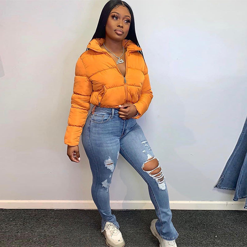 Woman wearing a vibrant orange cropped puffer parka jacket with a stand-up collar and full zip closure, paired with ripped blue jeans.