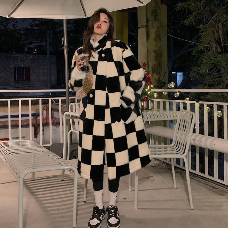 A woman wearing an elegant black and white checkerboard double-breasted long faux fur coat, showcasing its style and unique pattern.