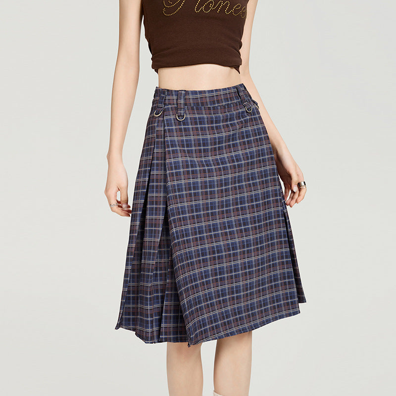 Woman wearing a blue plaid A-line pleated midi skirt, styled with a brown crop top and leg warmers, embodying college and Harajuku fashion.