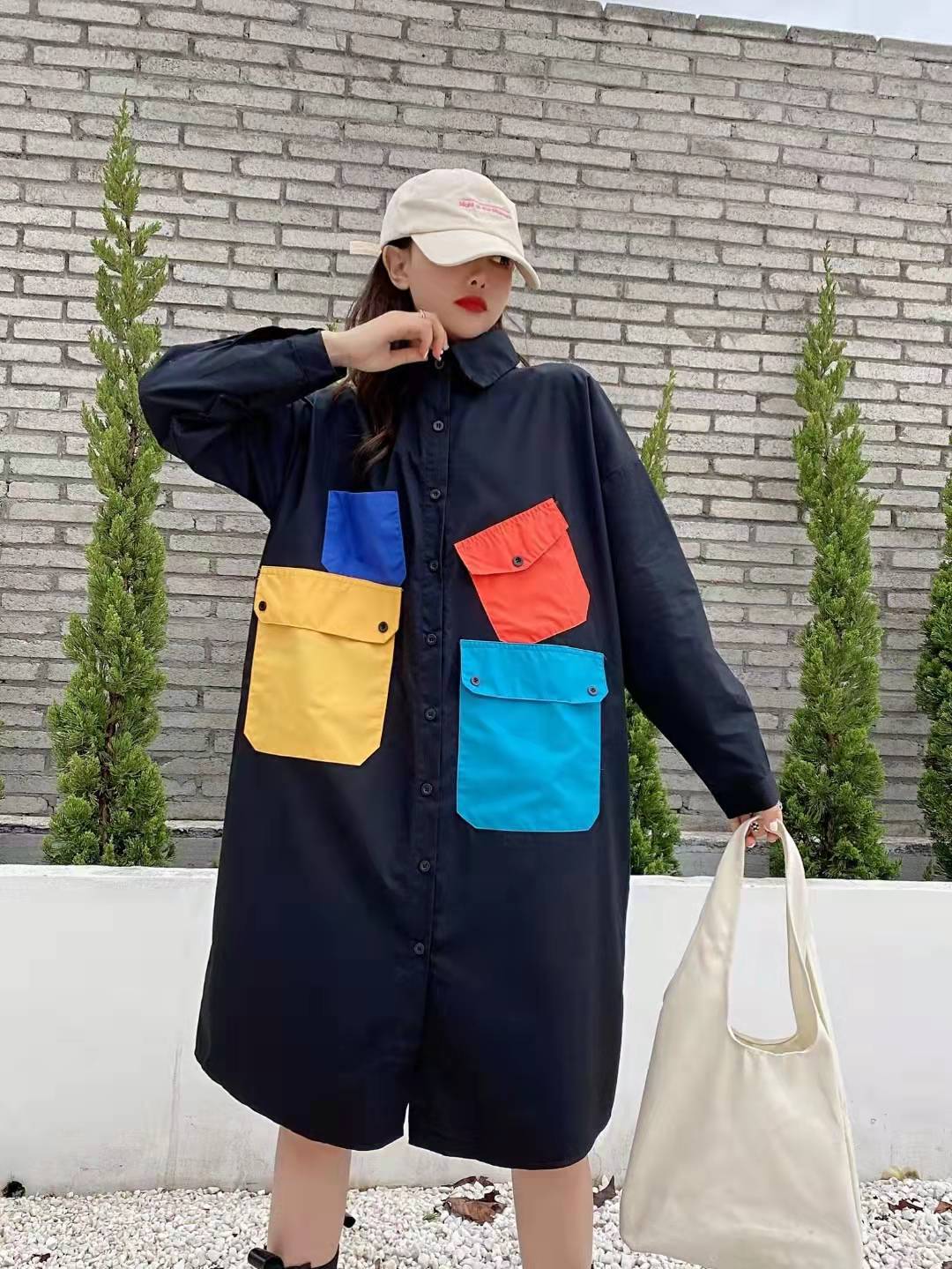 Model wearing a black long-sleeve, collared, button-front mini dress with square patchwork pockets in blue, yellow, and orange.