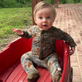 Camo print baby zippy in olive green, tan, and rust brown with fold-over cuffs.