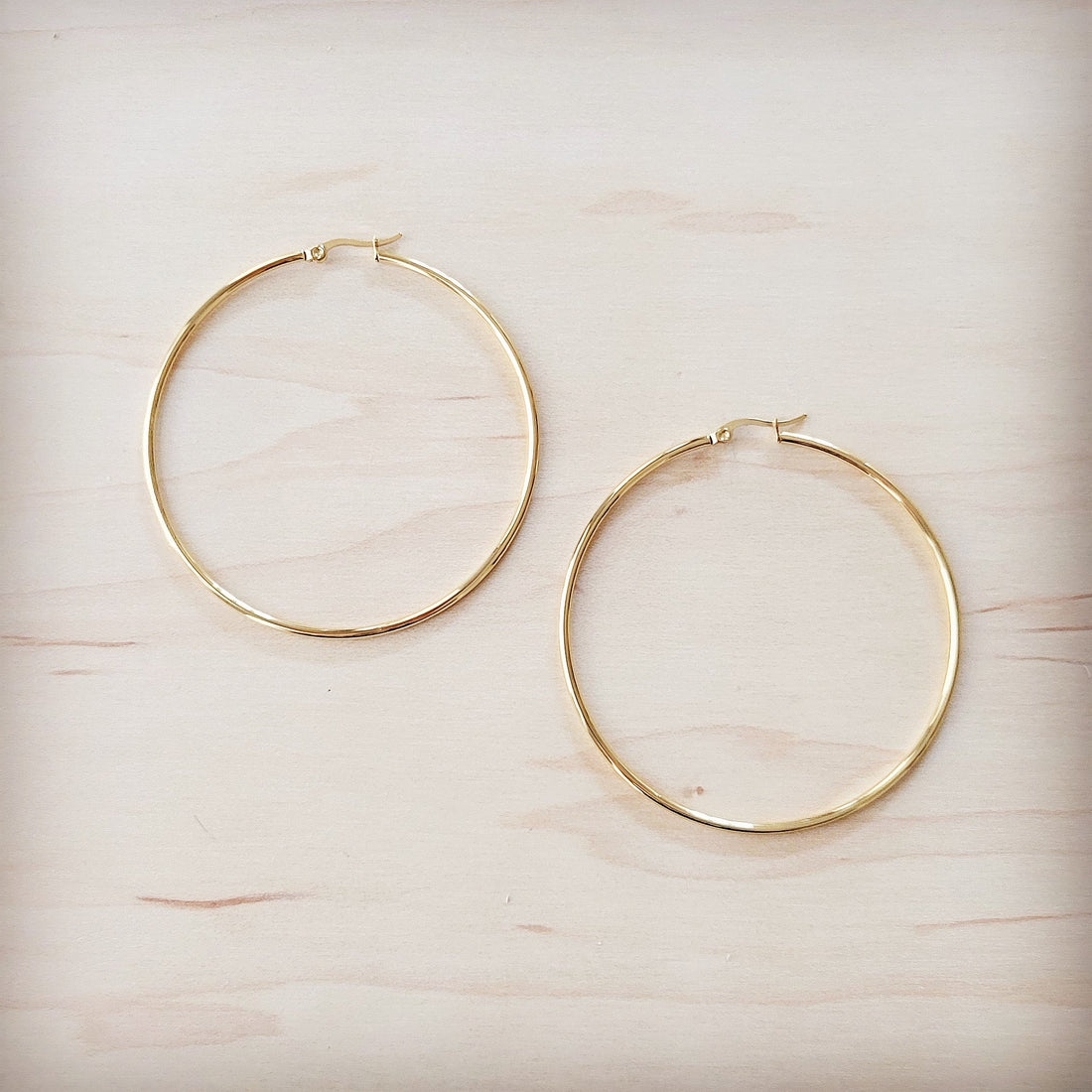 Extra large gold-tone stainless steel hoop earrings on a light wooden background