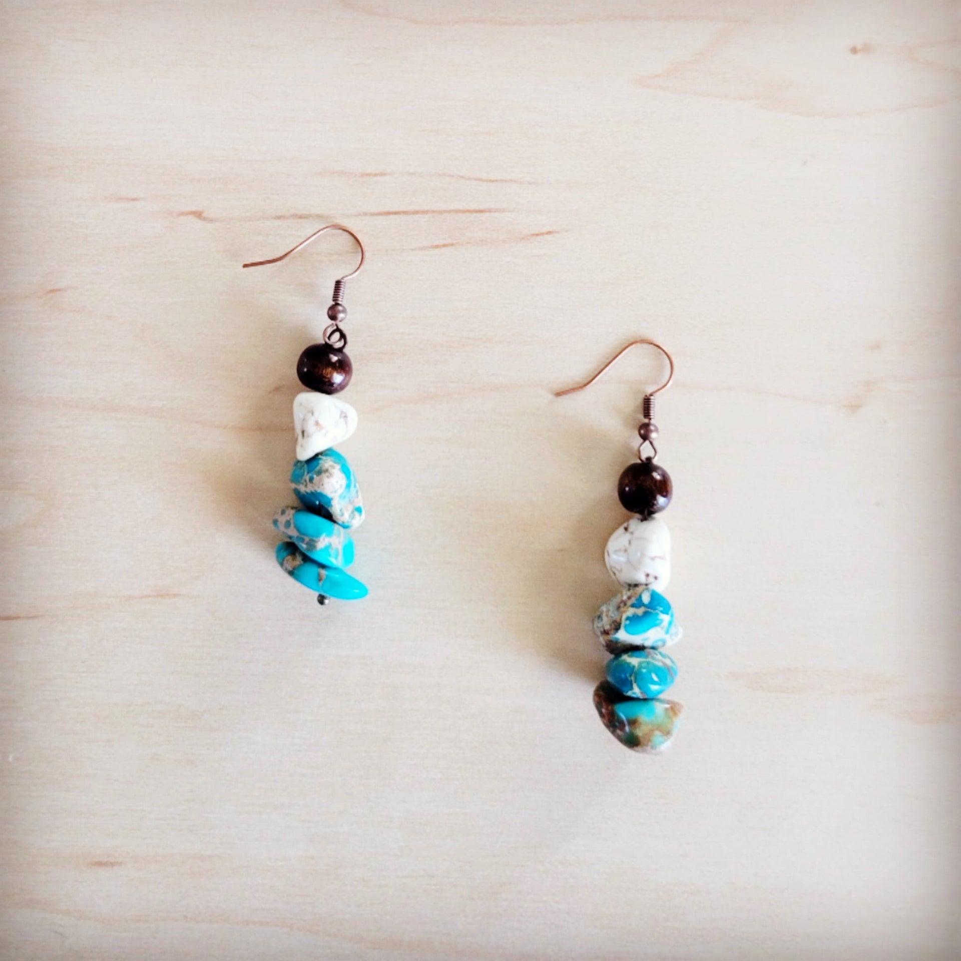 Handcrafted boho drop earrings featuring brown wood, white turquoise, and blue regalite stone beads on copper-tone hooks.