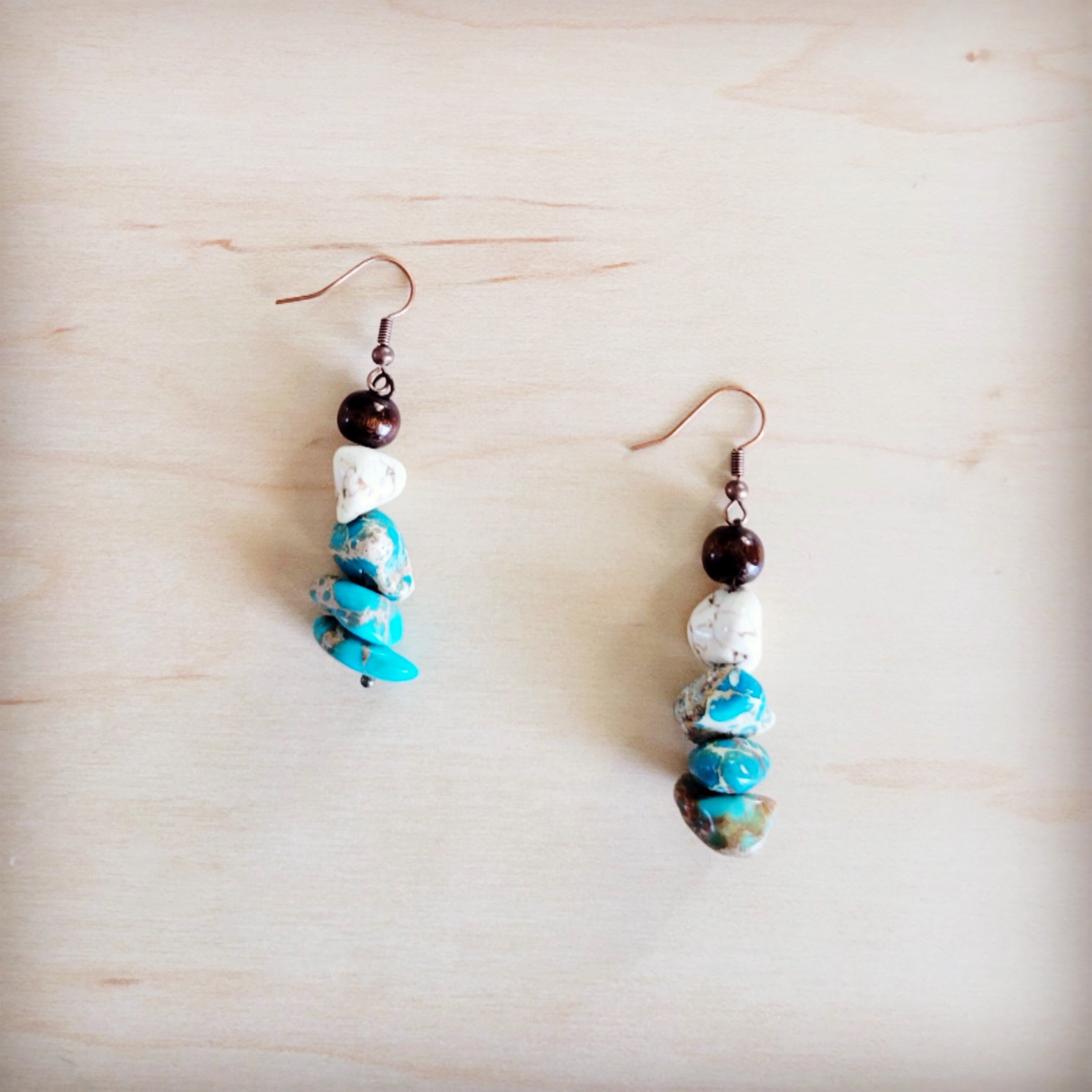 Handcrafted boho drop earrings featuring brown wood, white turquoise, and blue regalite stone beads on copper-tone hooks.