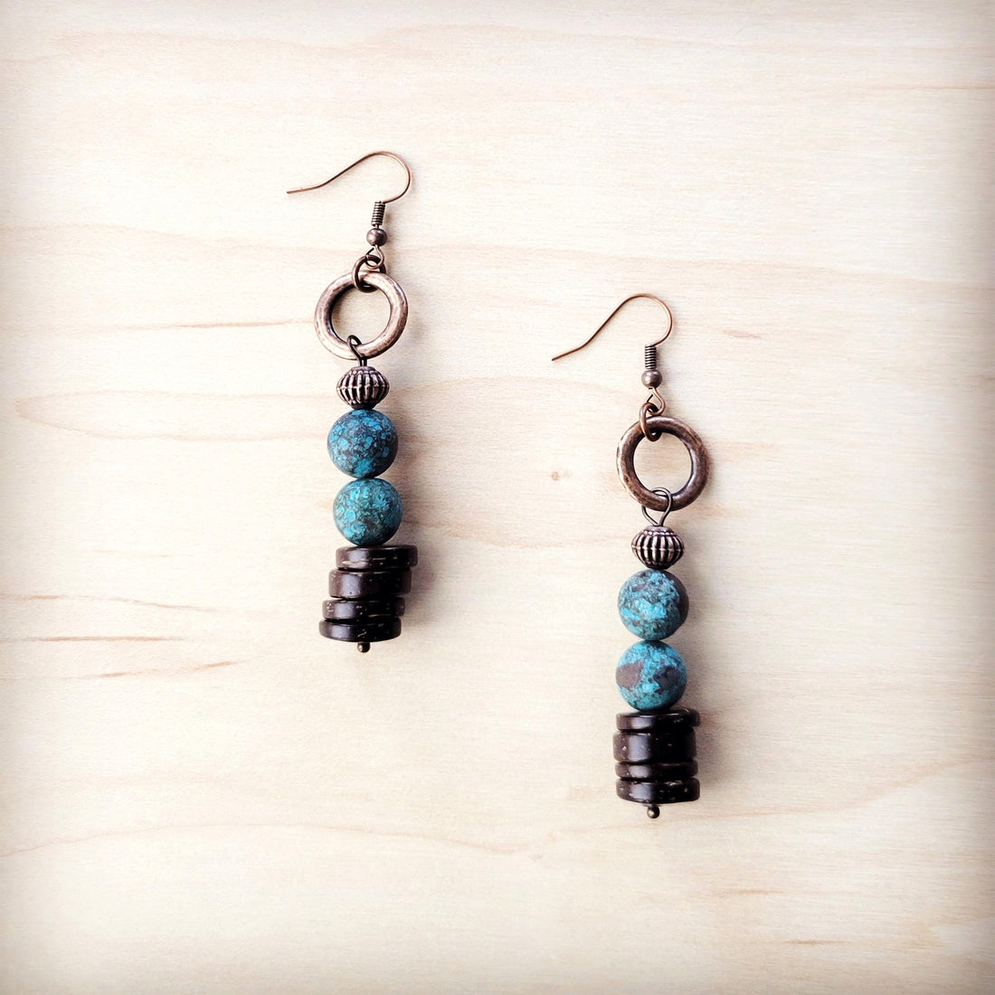 Natural American turquoise and dark wood bead drop earrings with copper-tone hook closures on a light wood background.