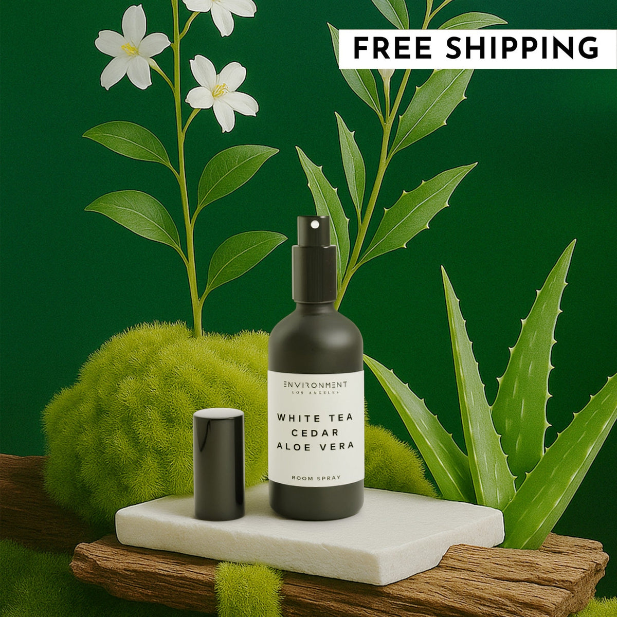 A dark glass bottle of White Tea, Cedar, and Aloe Vera room spray resting on a white stone tile surrounded by lush green foliage.