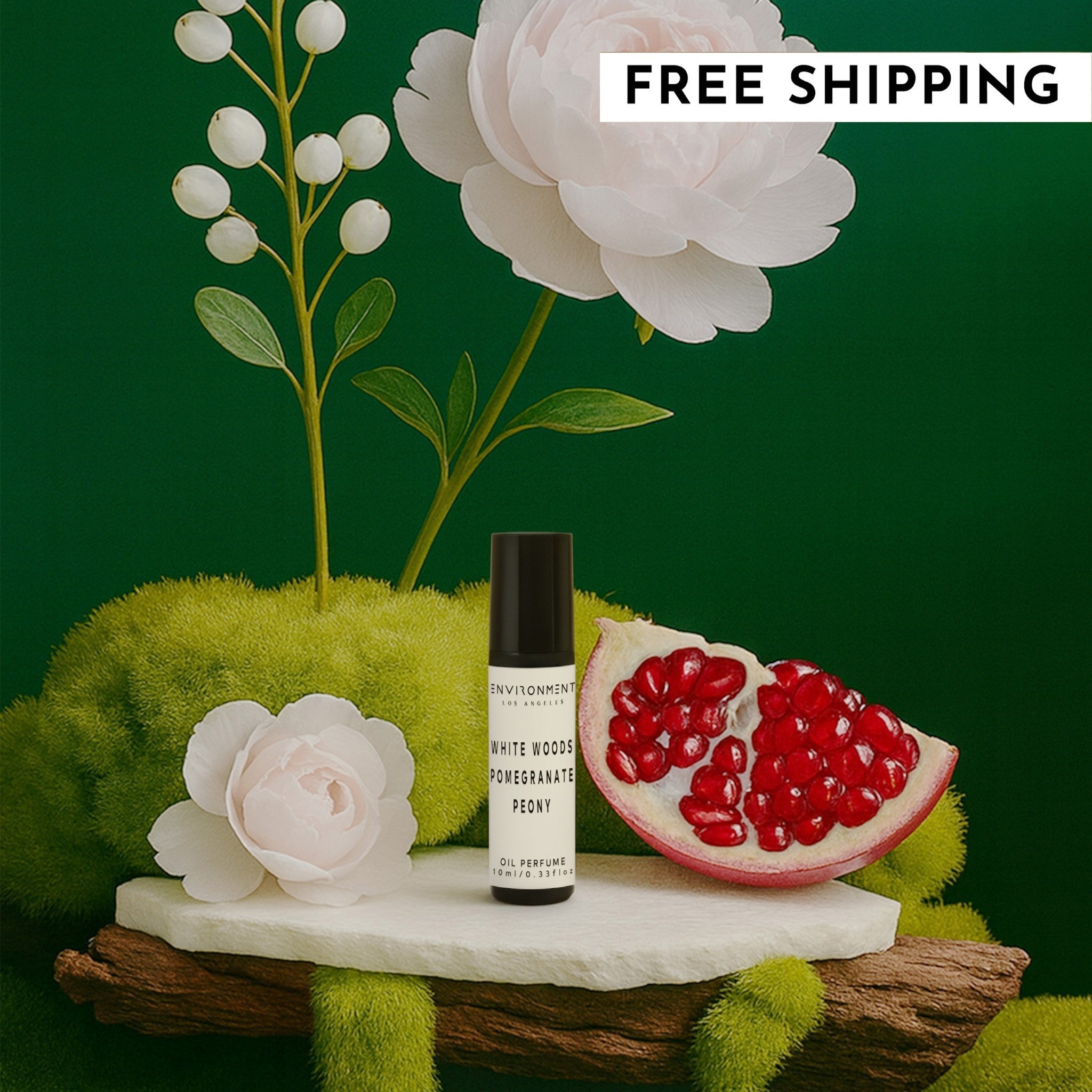 White Woods Pomegranate Peony roll-on oil perfume bottle displayed on a natural mossy stone surface with white flowers and pomegranate.