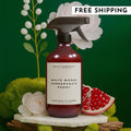 Bottle of White Woods Pomegranate Peony surface cleaner surrounded by natural moss, flowers, and fruit.
