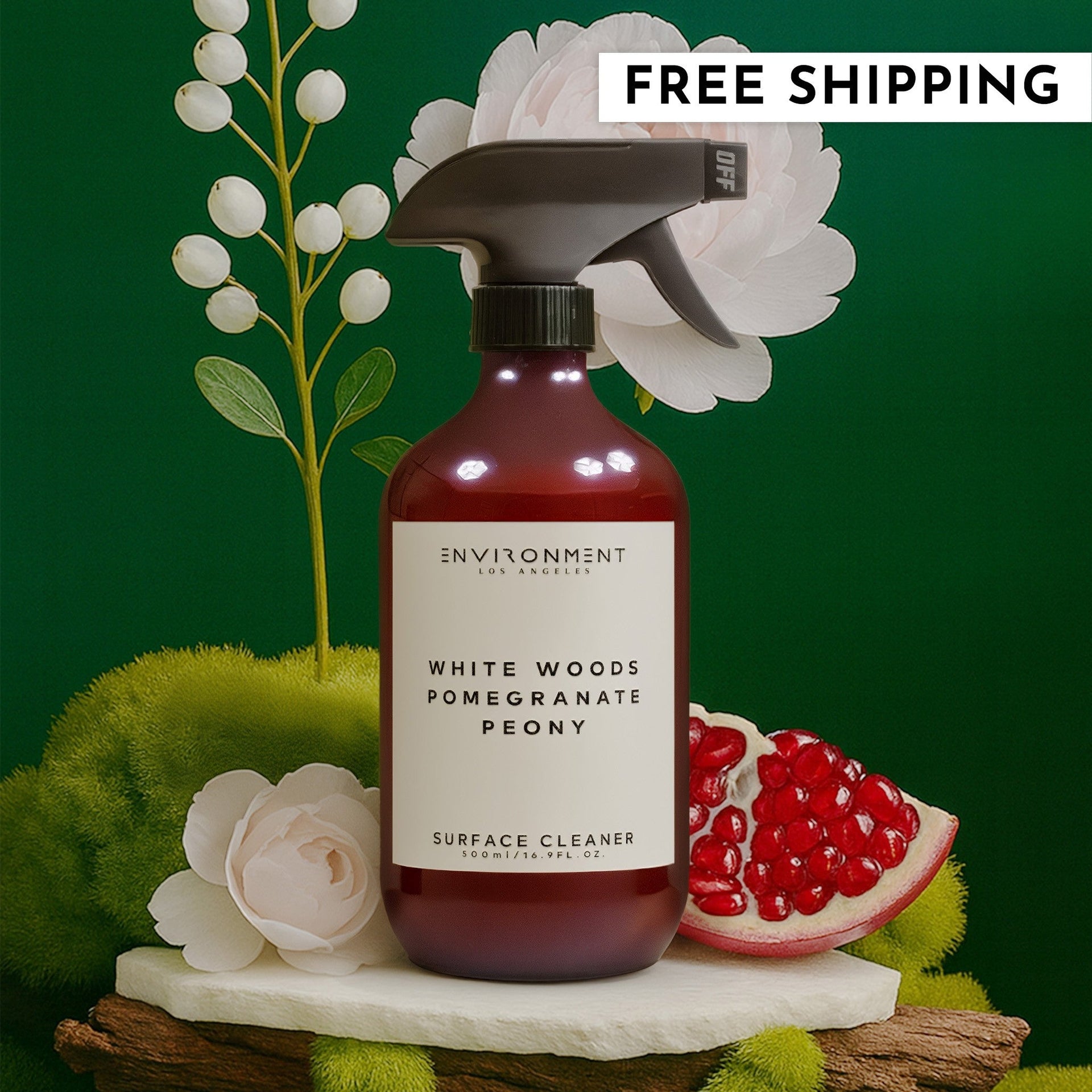 Bottle of White Woods Pomegranate Peony surface cleaner surrounded by natural moss, flowers, and fruit.