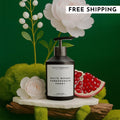 White Woods Pomegranate and Peony lotion bottle on a stone display with pomegranate fruit and white flowers
