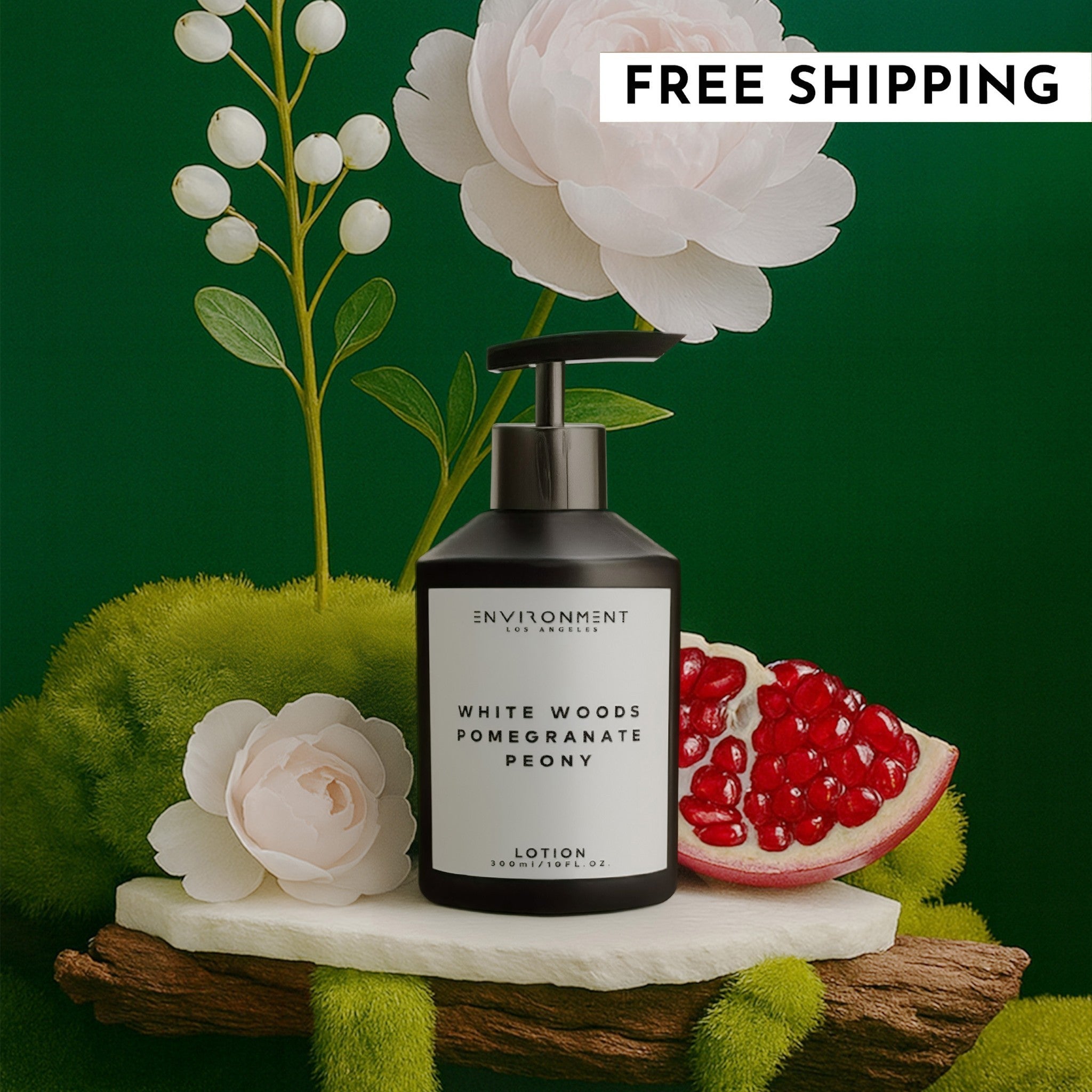 White Woods Pomegranate and Peony lotion bottle on a stone display with pomegranate fruit and white flowers