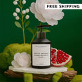 A bottle of White Woods Pomegranate Peony hand soap in a minimalist black bottle displayed in a lush, nature-inspired setting with pomegranate and peony flowers.
