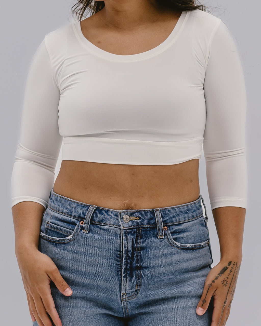 A woman wearing a 3/4 sleeve cropped layering top in a solid color