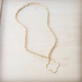 A matte gold-tone necklace with an open quatrefoil pendant hanging from an oval-link chain on a light wooden background.