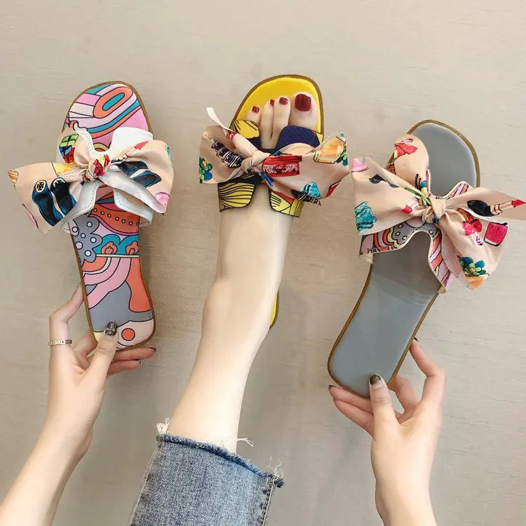 Colorful patterned women's flat slide sandals with a large decorative bow on the strap.