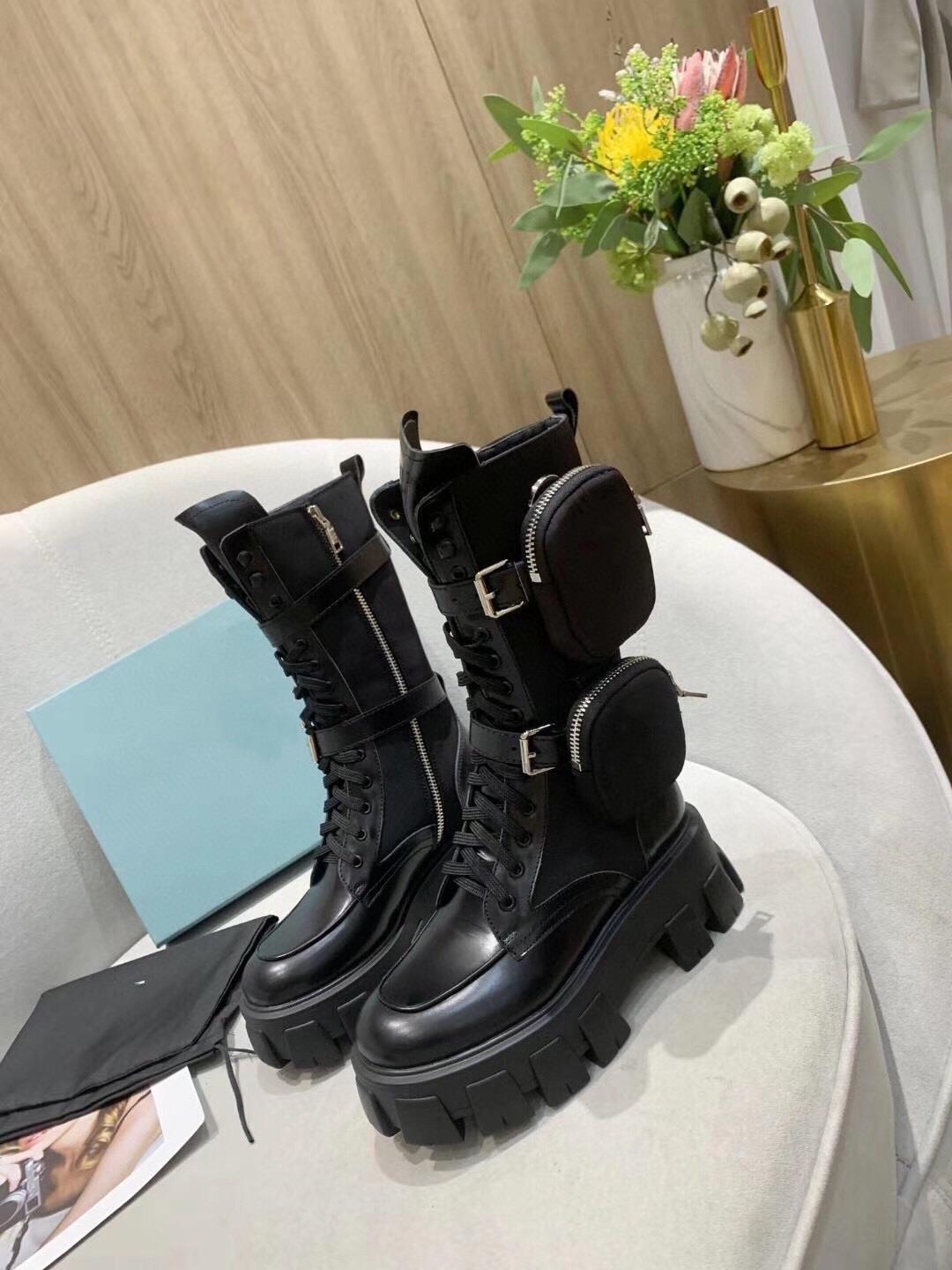 Women's black leather platform combat boots with chunky lug soles and detachable zippered pouches on a light sofa.