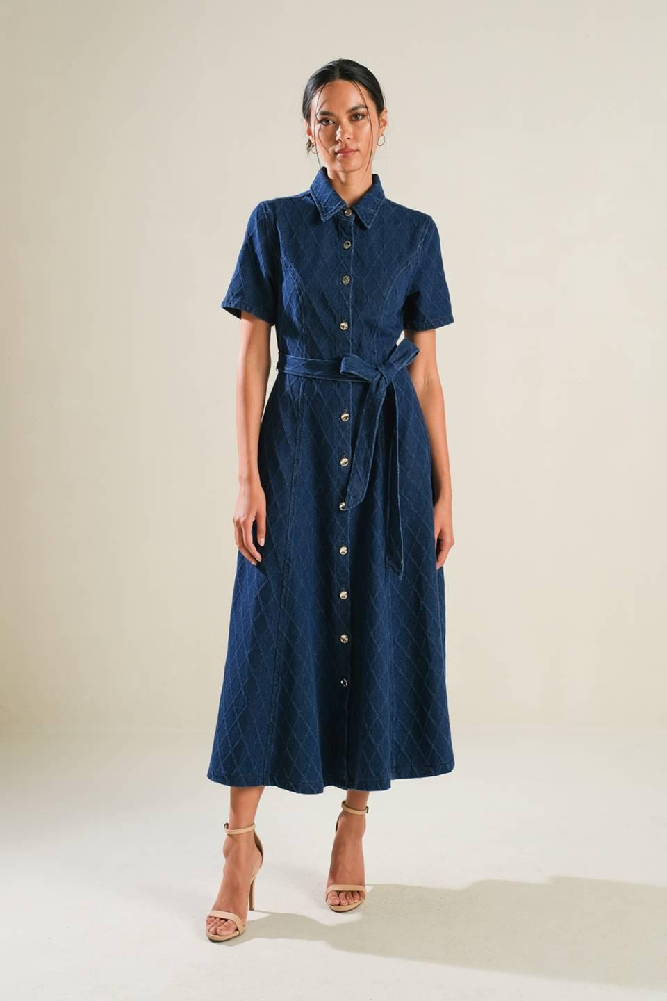 A woman wearing a blue textured denim midi dress with a collar, button front, and a self-tie sash.