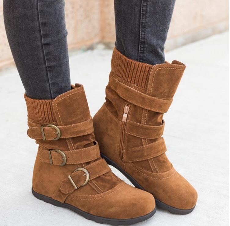 A pair of women's brown faux suede mid-calf boots featuring three decorative antique brass buckles and a cozy ribbed knit cuff, styled with dark denim jeans. Also available in black.