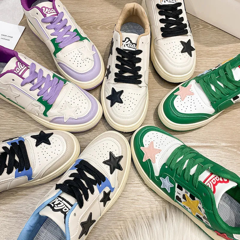 Collection of white athletic sneakers with contrasting green, purple, black, and blue accents, star patches, and round toes, displayed on a wooden floor.