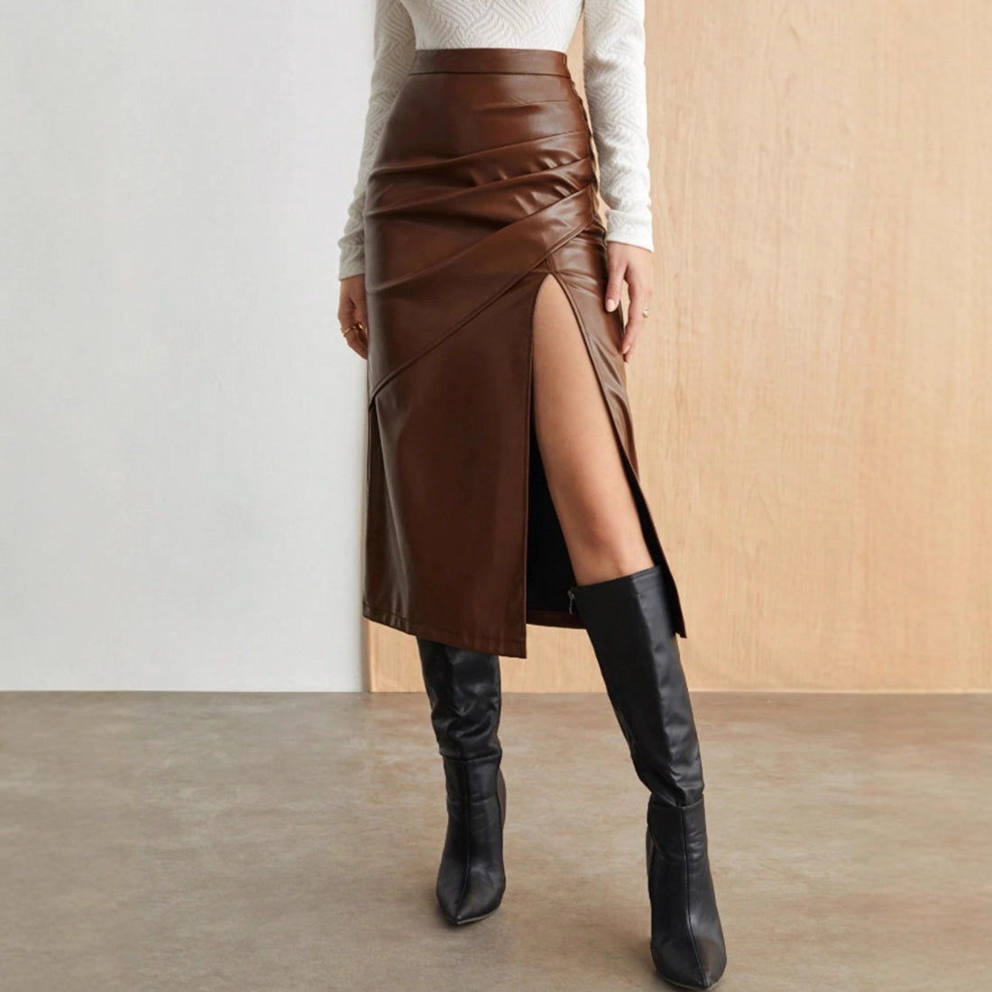 Model wearing a high-waisted faux leather midi skirt with a thigh-high side split and knee-high boots, available in brown and black.