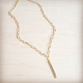 A gold-tone long chain necklace with a sleek vertical bar pendant resting on a light wooden surface.