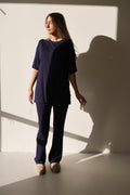 A woman wearing an oversized Blueberry Ribbed bamboo short sleeve top and matching flare pants while standing against a neutral wall.