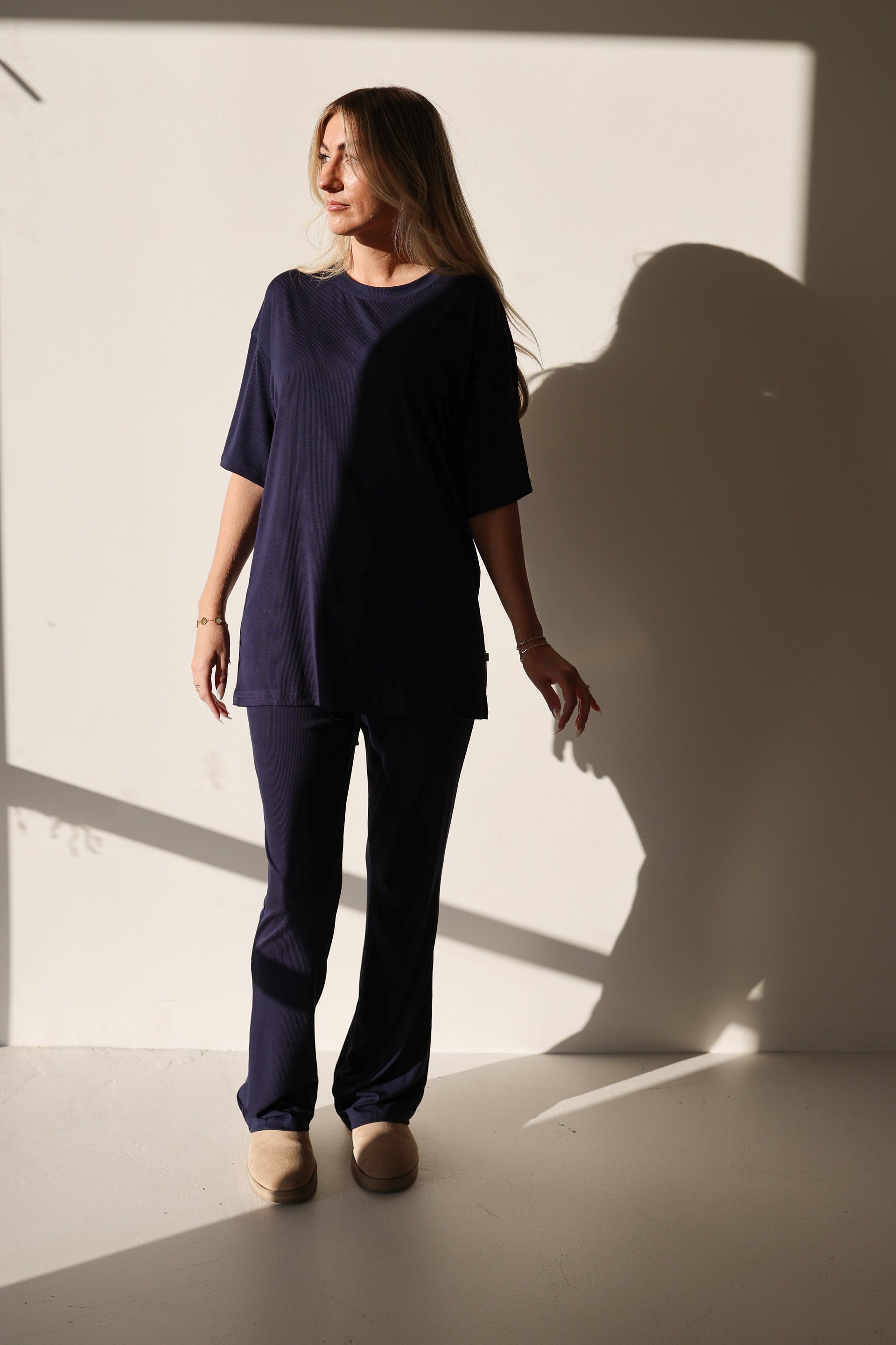A woman wearing an oversized Blueberry Ribbed bamboo short sleeve top and matching flare pants while standing against a neutral wall.