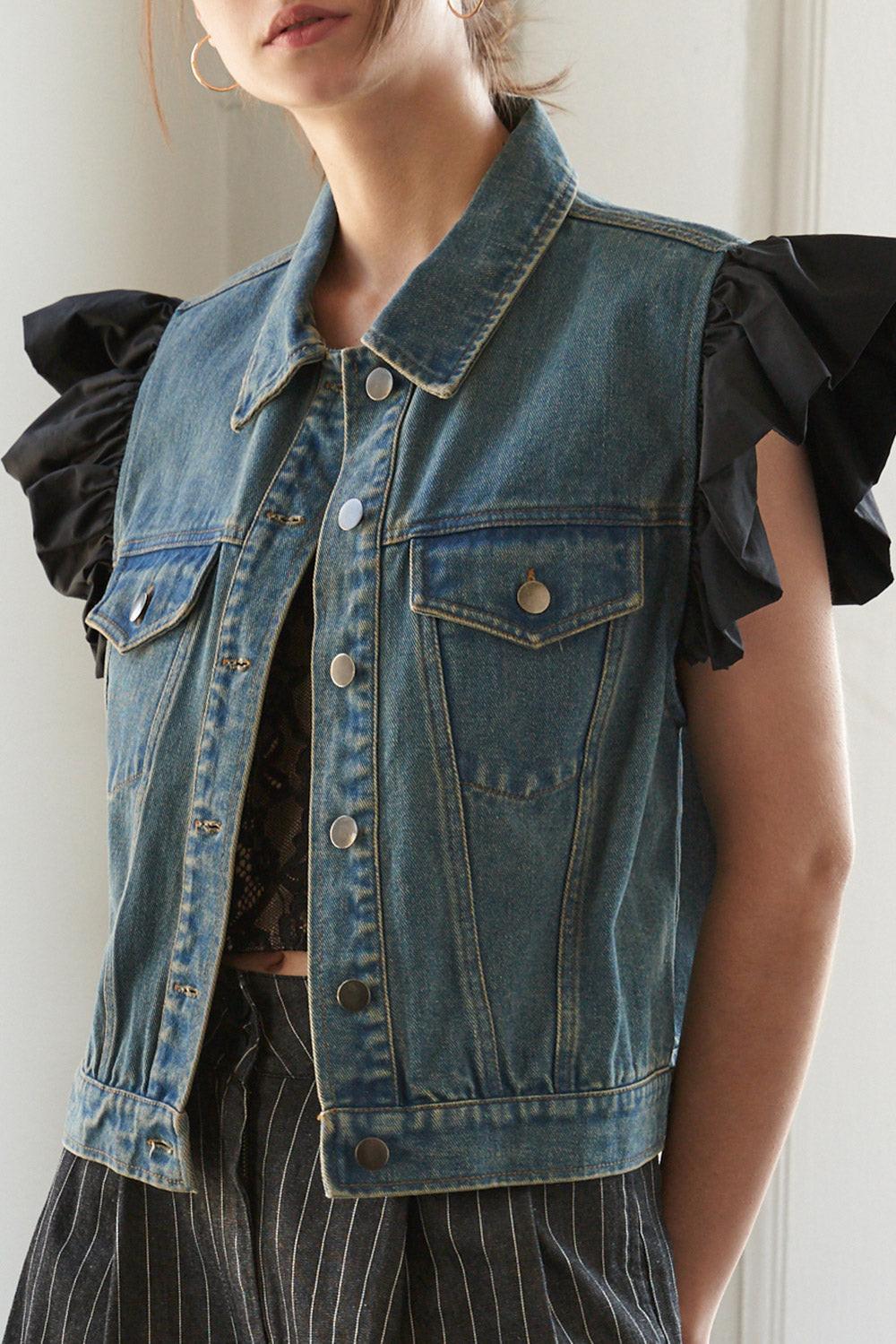 Model wearing a washed blue denim vest with black ruffled sleeves and silver button details.