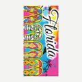 A colorful beach towel featuring a Florida-themed print with palm trees, a sunset, and multiple pairs of patterned flip-flops.