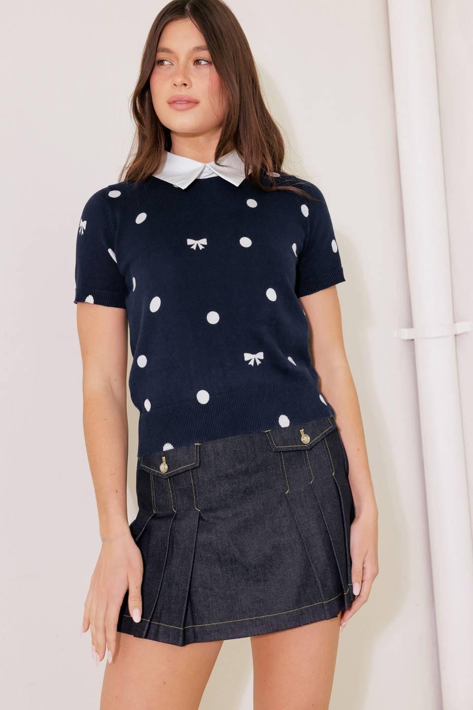 A woman wearing a navy blue sweater knit top with white polka dots, white bows, and a white collar.