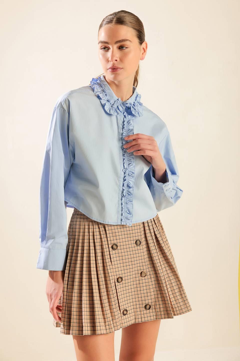 A light blue button-down woven top with a ruffled collar and placket worn by a model.
