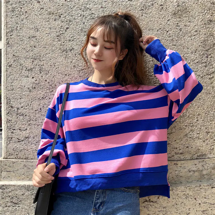 A woman wearing a vibrant pink and blue horizontal striped long-sleeve crewneck pullover.