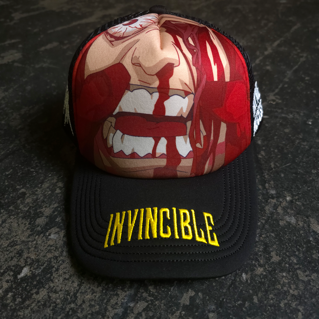 Close up front view of a black trucker hat with graphic artwork of a bloodied face and yellow Invincible embroidery on the brim