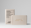 A beige fragrance-free cleansing bar next to its box packaging, labeled as a face and body cleansing bar for sensitive skin.